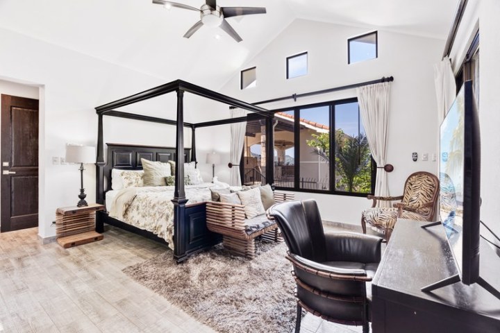 Spacious bedroom with canopy bed, large windows, and modern furniture.