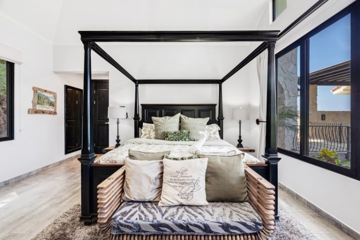 Bedroom with a four-poster bed, decorative pillows, and large windows.