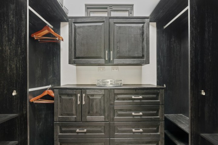 Modern walk-in closet with dark wood cabinetry and hanging rods.