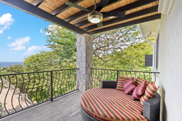Outdoor terrace with round daybed, striped cushions, ceiling fan, and tree views.