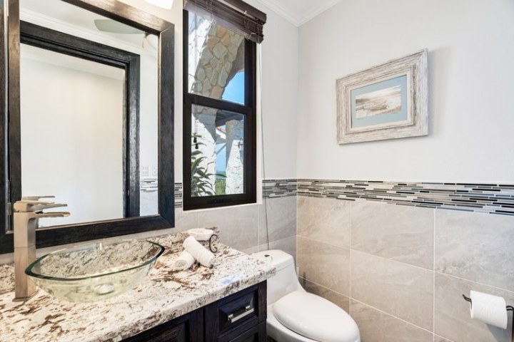 Bathroom with glass sink, large mirror, and framed artwork on tiled wall.