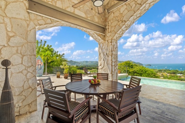 Outdoor patio with round table, six chairs, ocean view, and infinity pool.