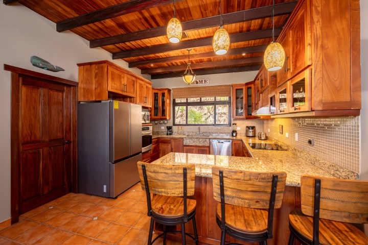 Wooden kitchen with granite countertops, bar seating, and hanging lights.