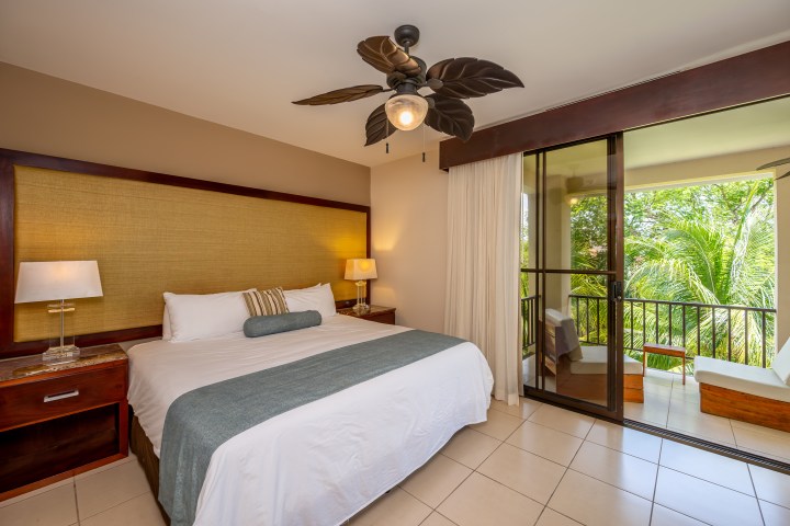 Cozy bedroom with king bed, ceiling fan, and balcony view.