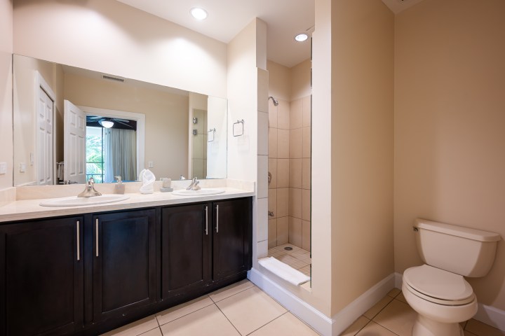 Modern bathroom with dark wood vanity, large mirror, shower, and toilet.