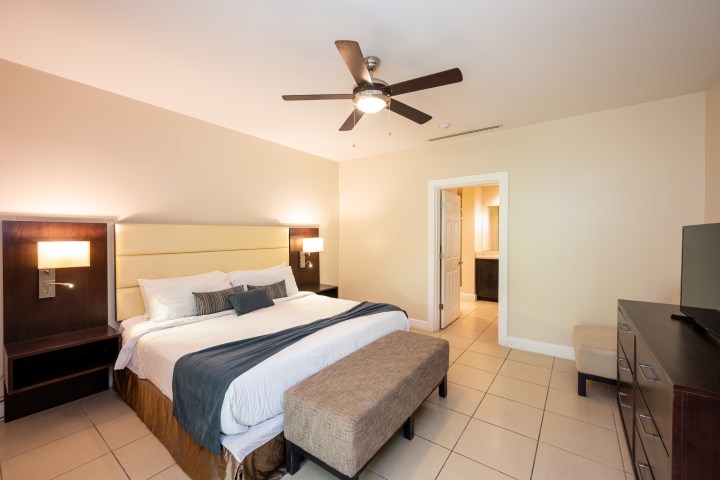 Modern bedroom with bed, ceiling fan, TV, dresser, and bathroom door.