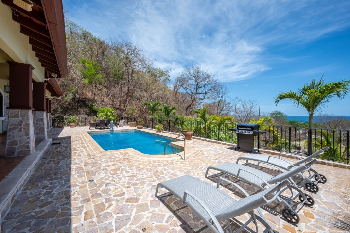 Outdoor pool patio with lounge chairs, grill, and ocean view.