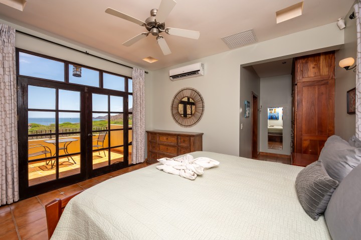 Bedroom with balcony view, bed, dresser, wall decor, and sliding glass doors.