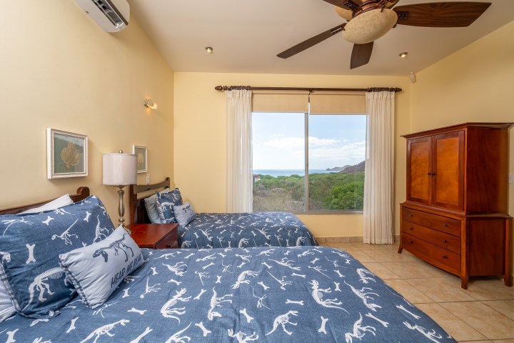 Bedroom with two beds, ocean view window, ceiling fan, and wooden furniture.