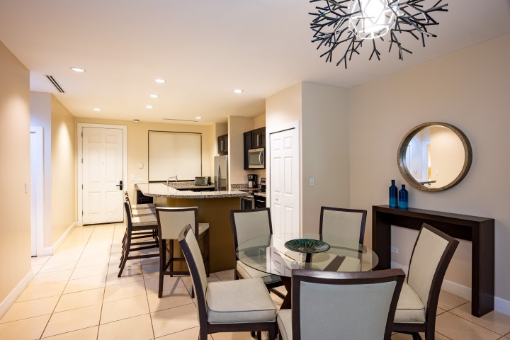 Modern dining room with round table, eight chairs, and a kitchen in the background.