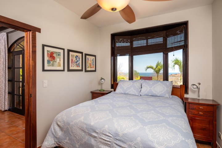 Cozy bedroom with a bed, three framed pictures, and a window with a view of trees.