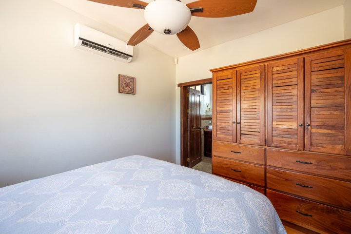Bedroom with wooden wardrobe, ceiling fan, and patterned bedspread.