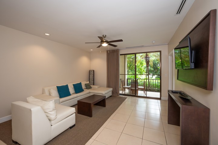 Living room with white sofa, blue cushions, TV, and sliding door to a patio with outdoor seating.