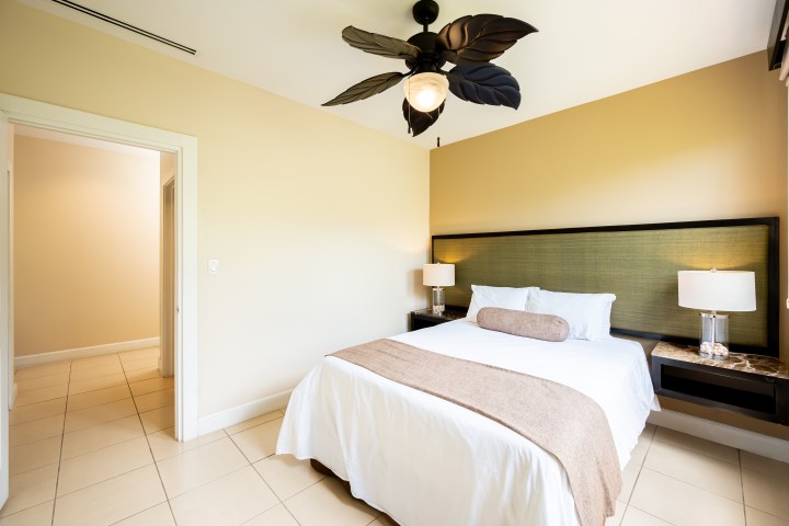 Bedroom with a bed, cushions, two lamps, and a ceiling fan with leaf-shaped blades.