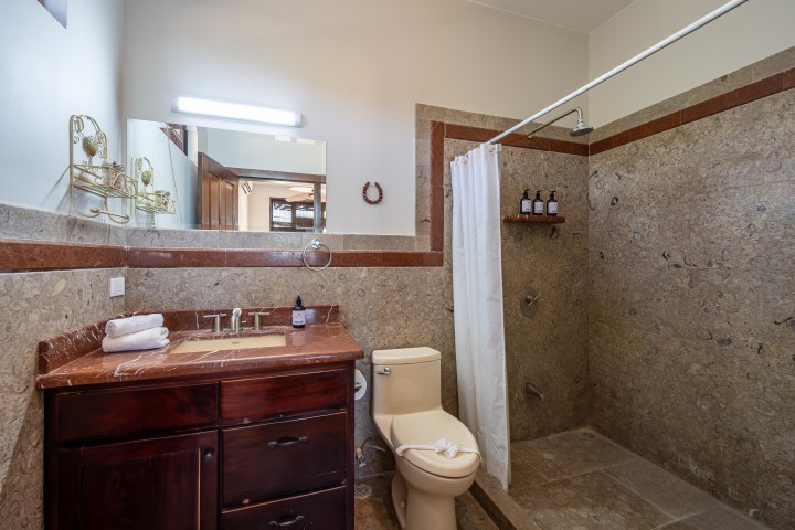 Modern bathroom with shower, vanity, and toilet on tan tiled floor.