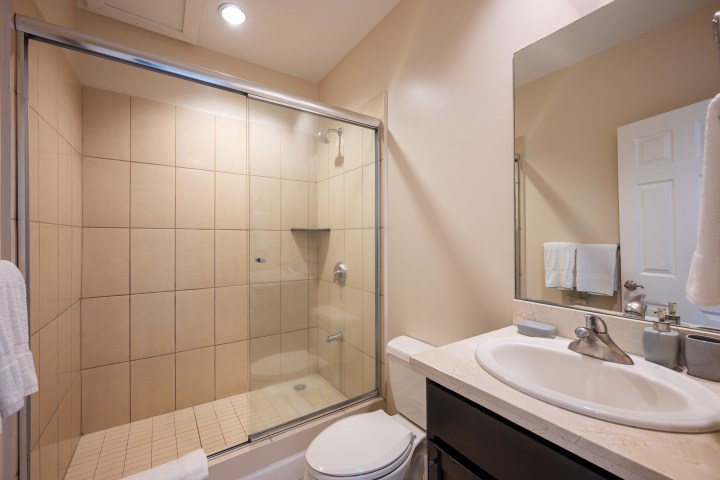 Modern bathroom with glass shower, beige tiles, sink, and mirror.