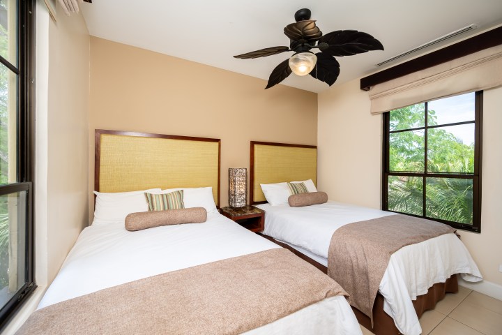 Two beds in a room with a ceiling fan and window view.