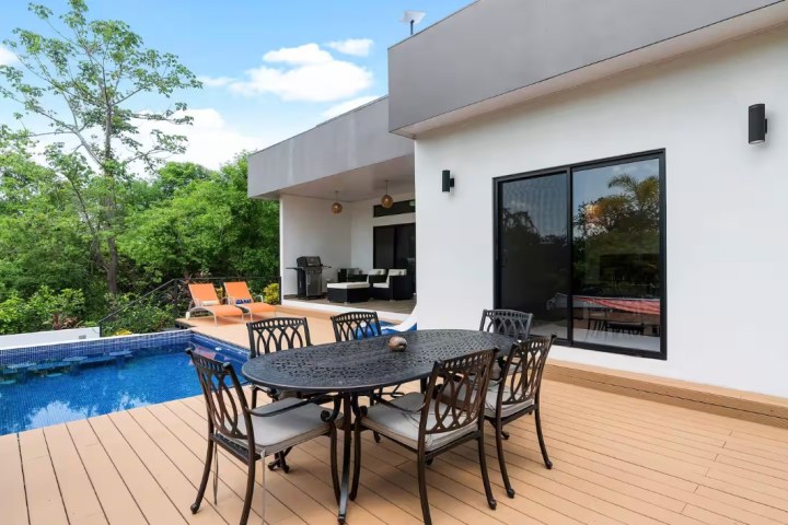 Modern patio with table, chairs, and pool next to white building.