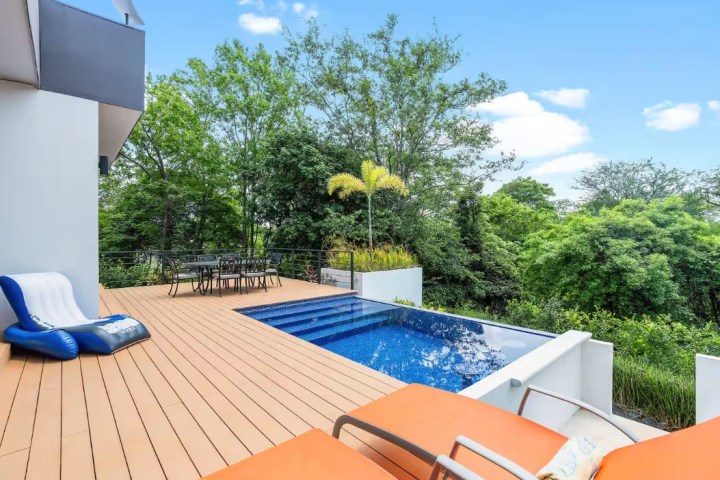 Outdoor deck with chairs, a small pool, and trees in the background.