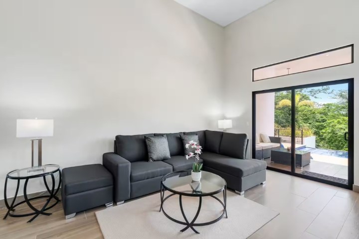 Modern living room with gray sectional sofa, round glass coffee table, and sliding glass doors to a patio.