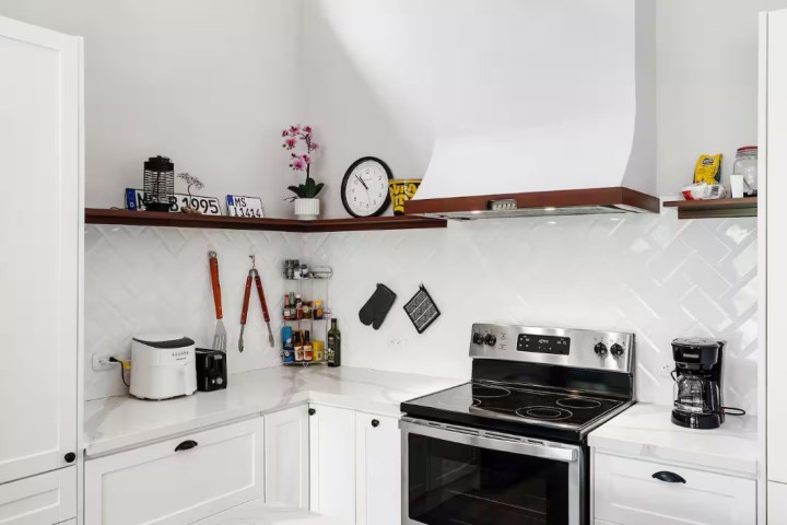 Modern kitchen with white cabinets, stovetop, and shelves with decor above.