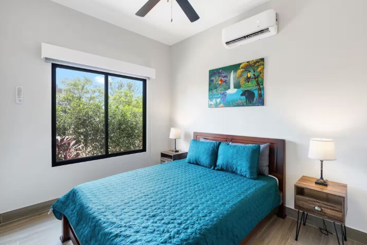 Bedroom with teal bedding, window view of trees, ceiling fan, and wall art above bed.