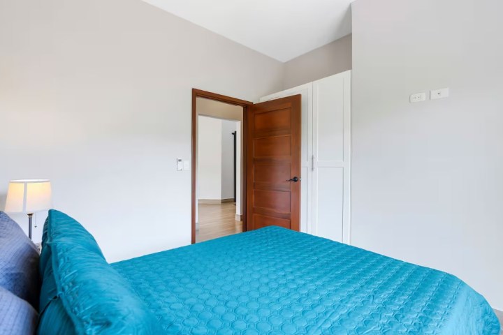 Bedroom with a teal bedspread, wooden door, lamp, and white walls.