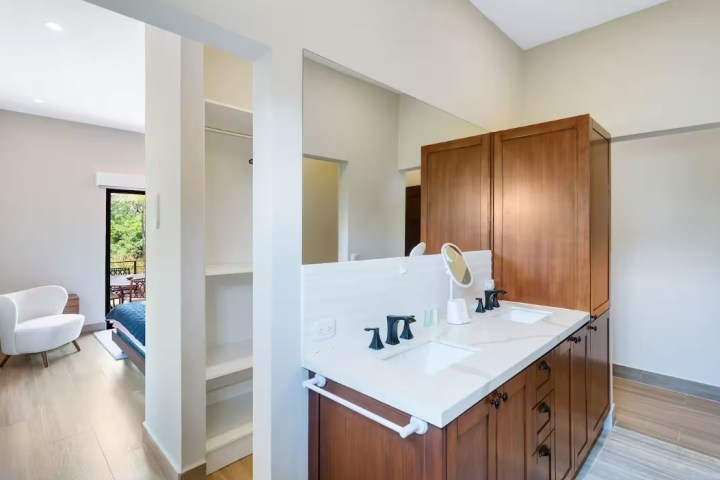 Modern bathroom with double sink and wooden cabinets, adjoining a bright bedroom.