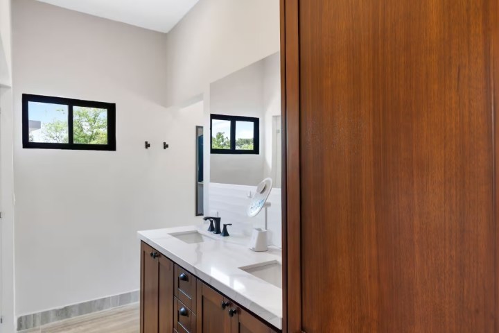 Bathroom with double sink vanity, mirror, and small windows.