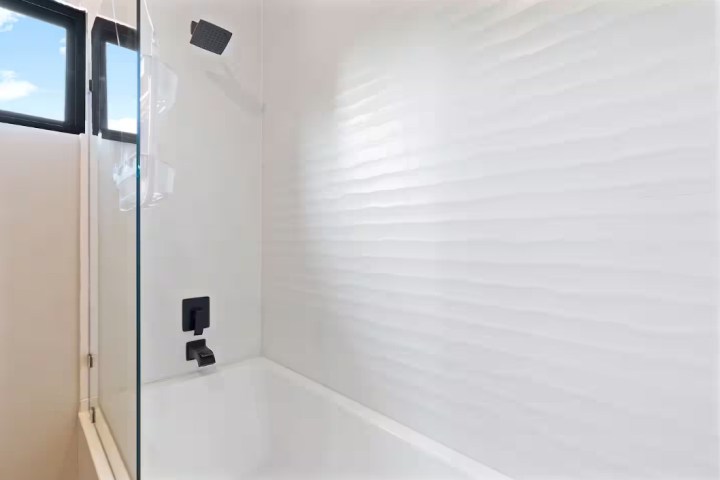 Modern bathroom with white tiles, black fixtures, and a glass shower screen.