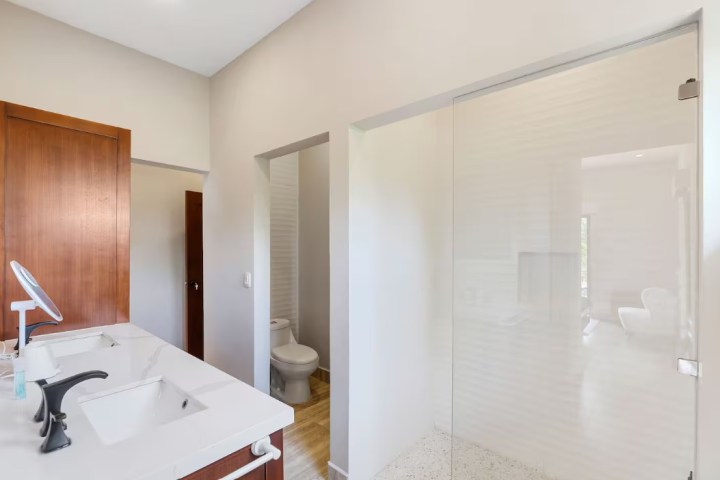 Modern bathroom with double sink vanity, shower, and toilet.