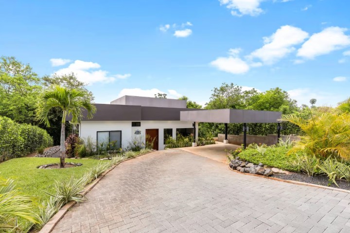 Modern house with flat roof, driveway, and tropical landscaping.