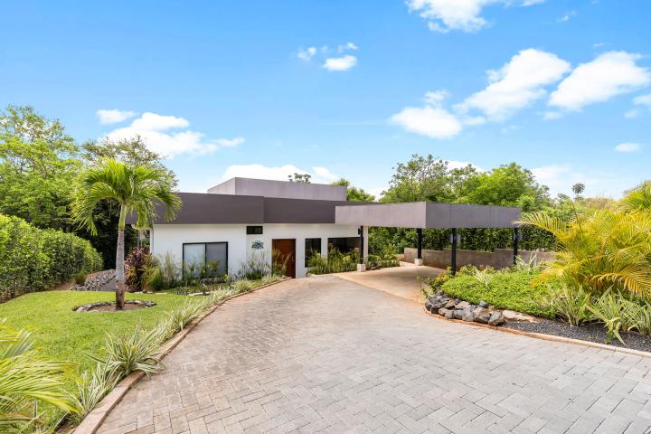 Modern house with flat roof, driveway, and lush greenery.
