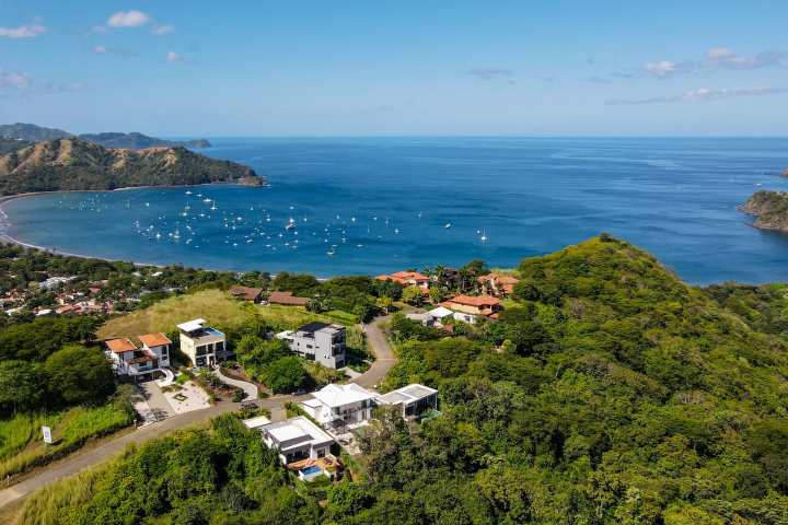 Aerial view of a coastal town with a bay, boats, and lush green hills.