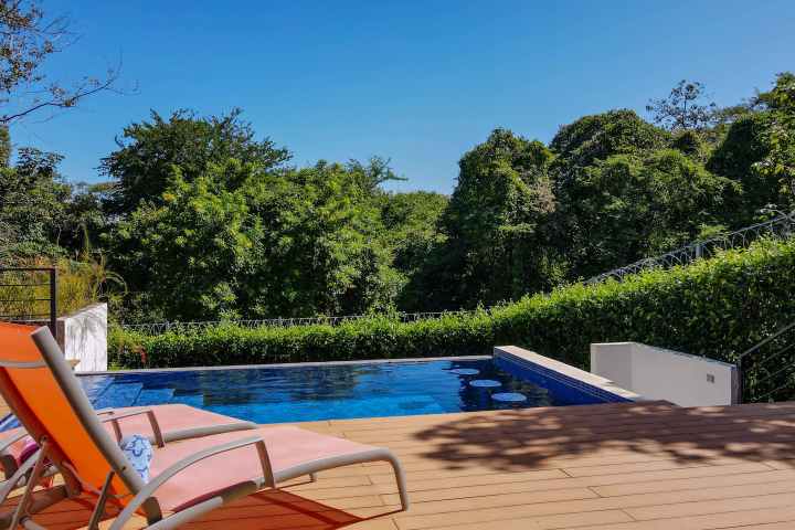 Two lounge chairs by a pool with lush greenery in the background.