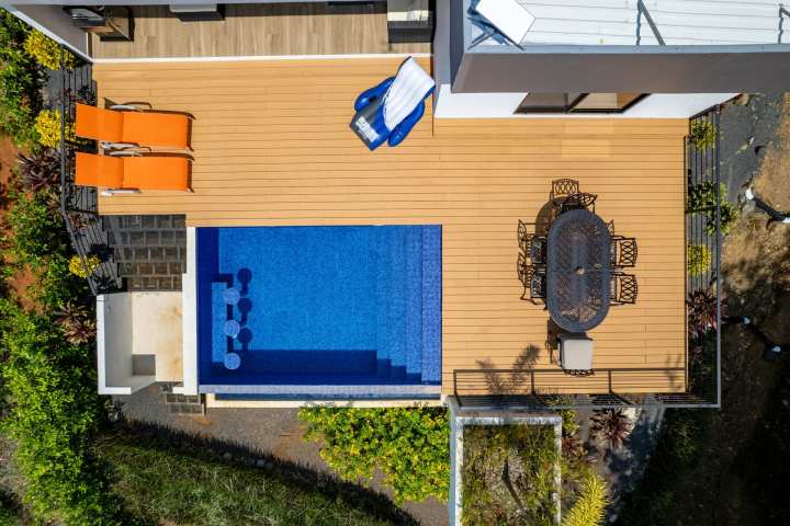Aerial view of a wooden deck with pool, two orange chairs, and a dining set.
