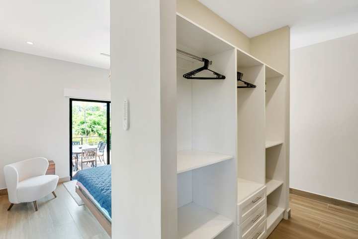 Modern bedroom with open closet, chair, and open sliding door to a balcony.