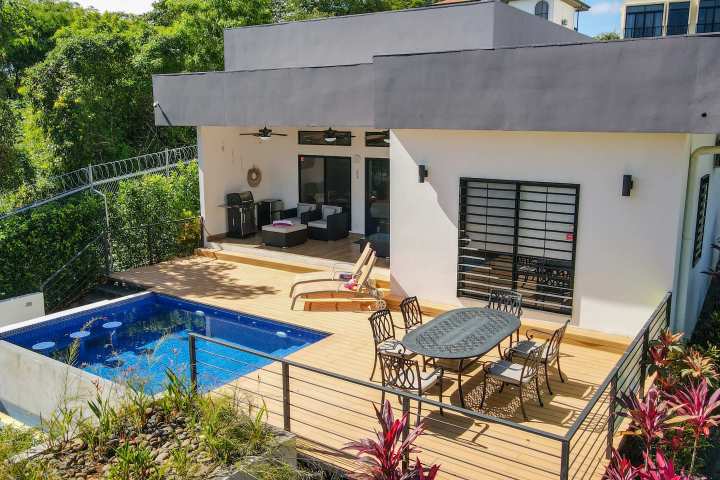 Modern house with a pool, patio furniture, and lush greenery.