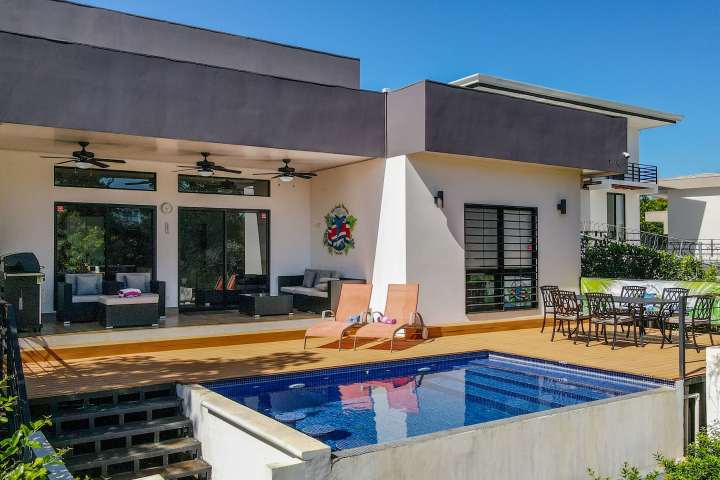 Modern house with pool, patio furniture, and clear blue sky.