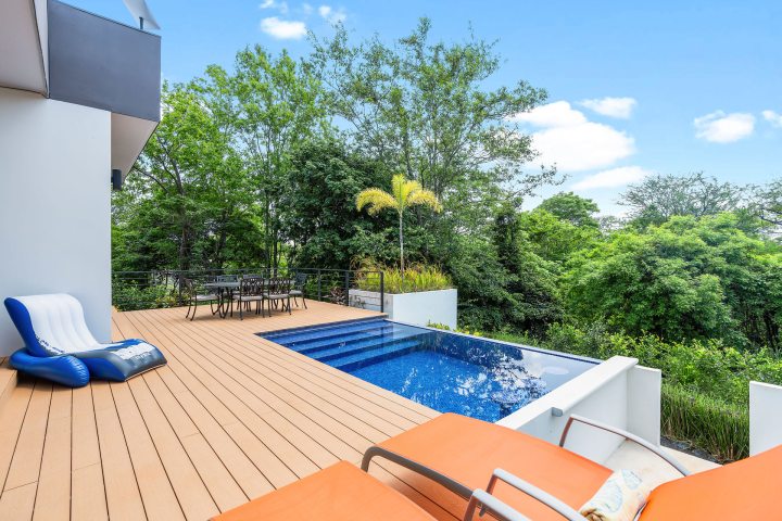 Modern patio with pool, orange loungers, and greenery.