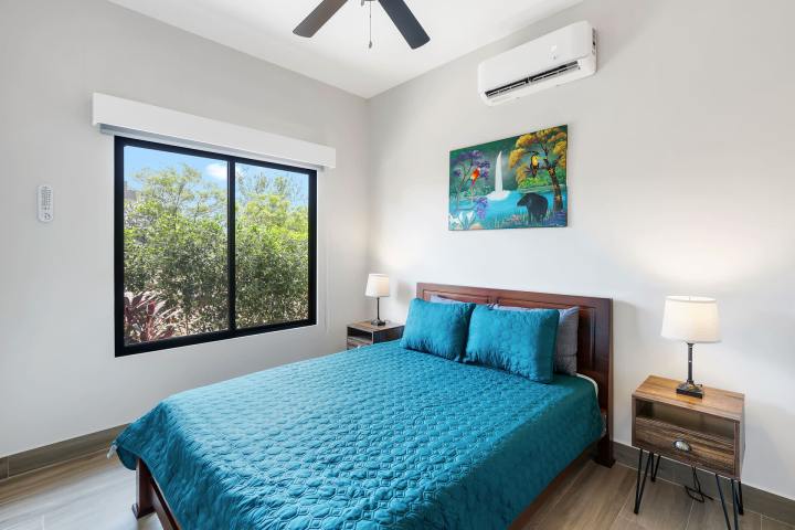 Bedroom with a blue bedspread, two lamps, window, painting, and ceiling fan.