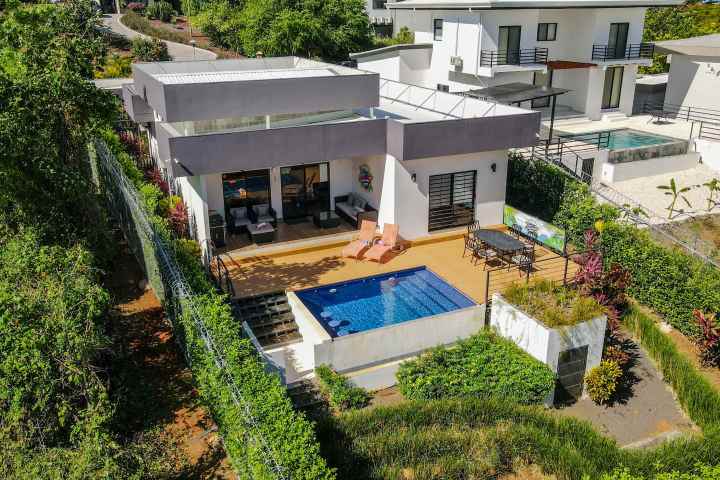Modern house with pool surrounded by greenery and other homes.