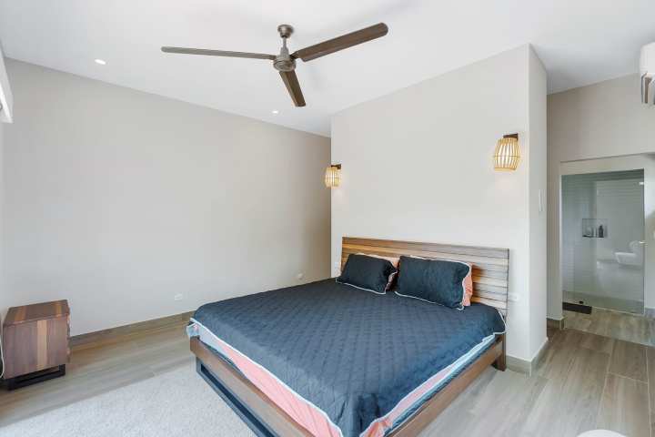 Modern bedroom with a black bedspread, wooden accents, ceiling fan, and a small bathroom visible.