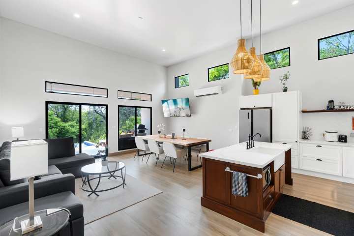 Modern open-plan living room with kitchen, island, dining table, and large windows.