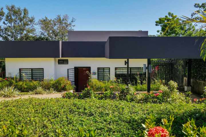 Modern house with flat roof, surrounded by lush greenery and garden.
