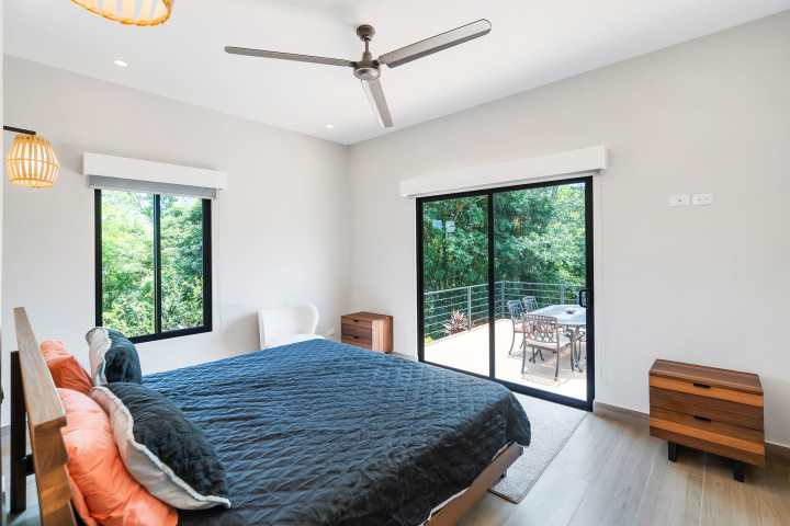 Modern bedroom with ceiling fan, large window, and sliding door to balcony.