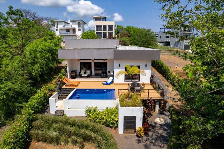 Modern villa with a pool, surrounded by greenery, set in a residential neighborhood.