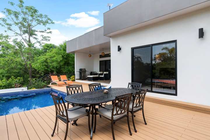 Modern patio with pool, table, chairs, and greenery.