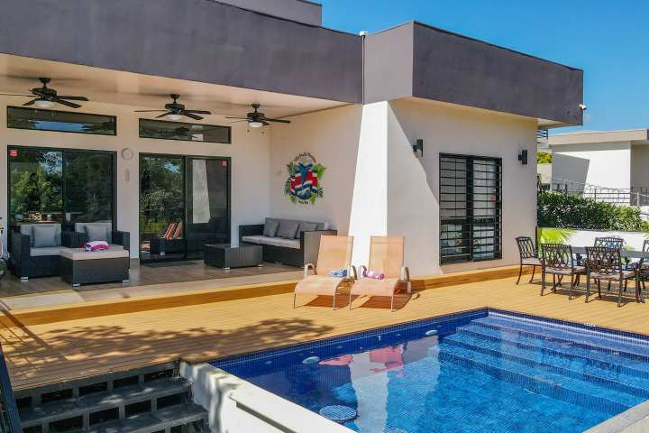 Modern patio with pool, loungers, sofa, and dining set under clear blue sky.