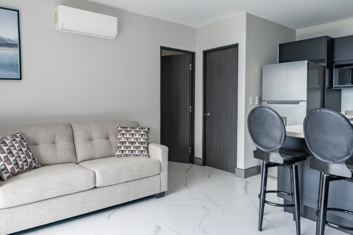 Modern living room with a sofa, framed art, and open kitchen area with barstools and appliances.